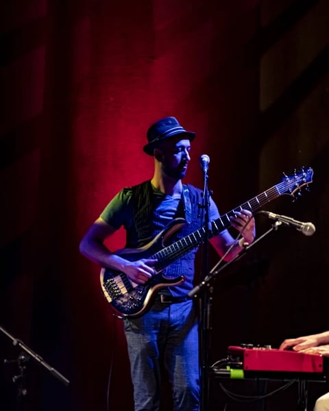 Musician playing bass guitar on stage under blue and red lighting