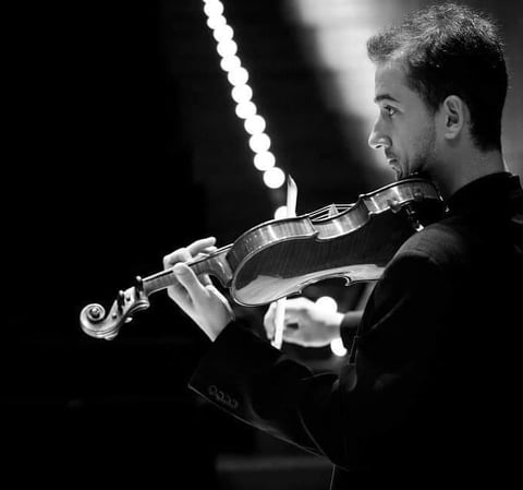 Violinist in formal attire playing against dark background